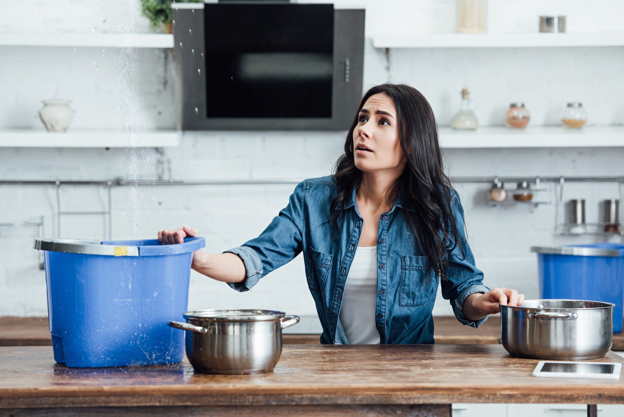 Confused brunette woman dealing with water damage in kitchen