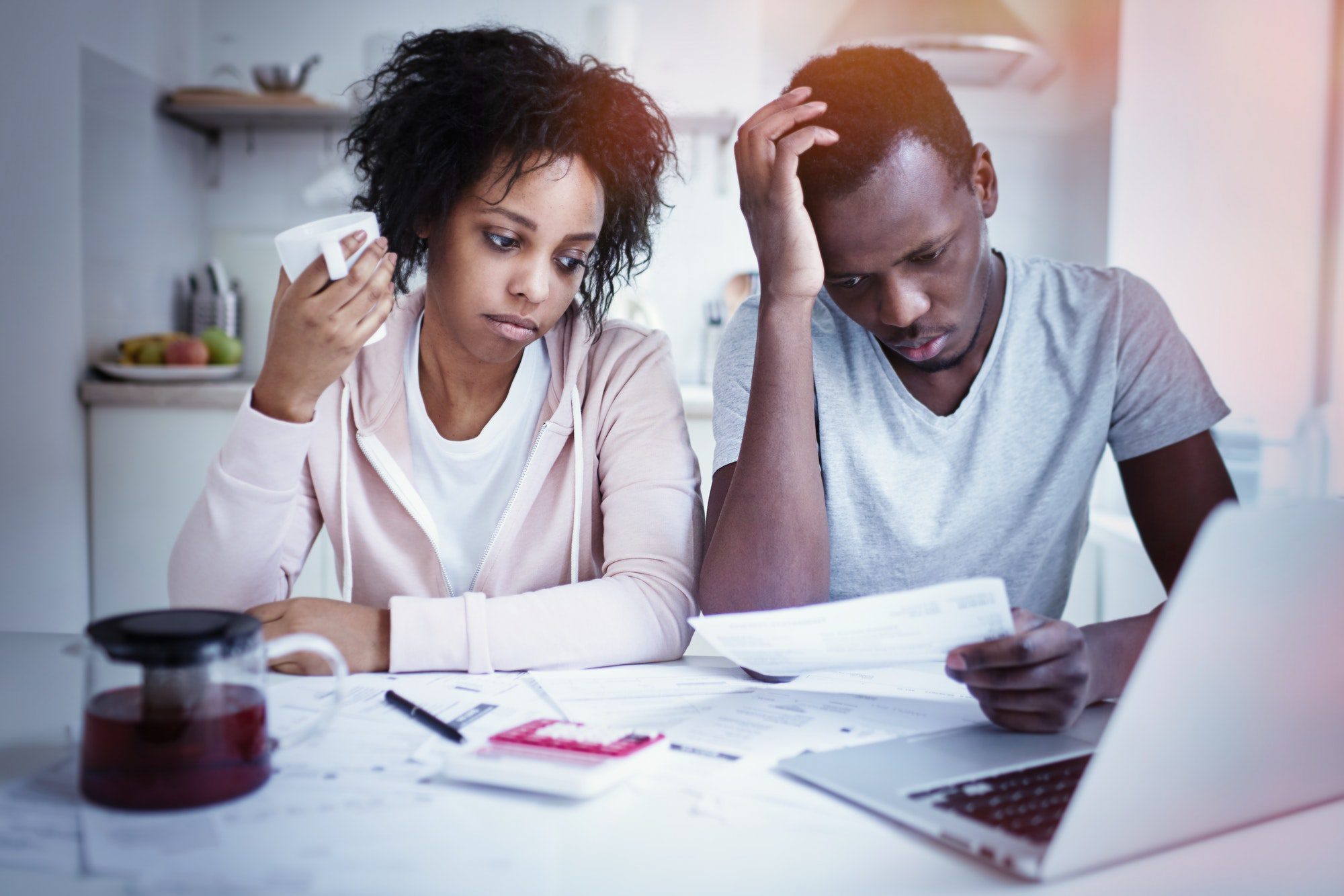 Unhappy couple reviewing their finances, making calculations with papers and laptop