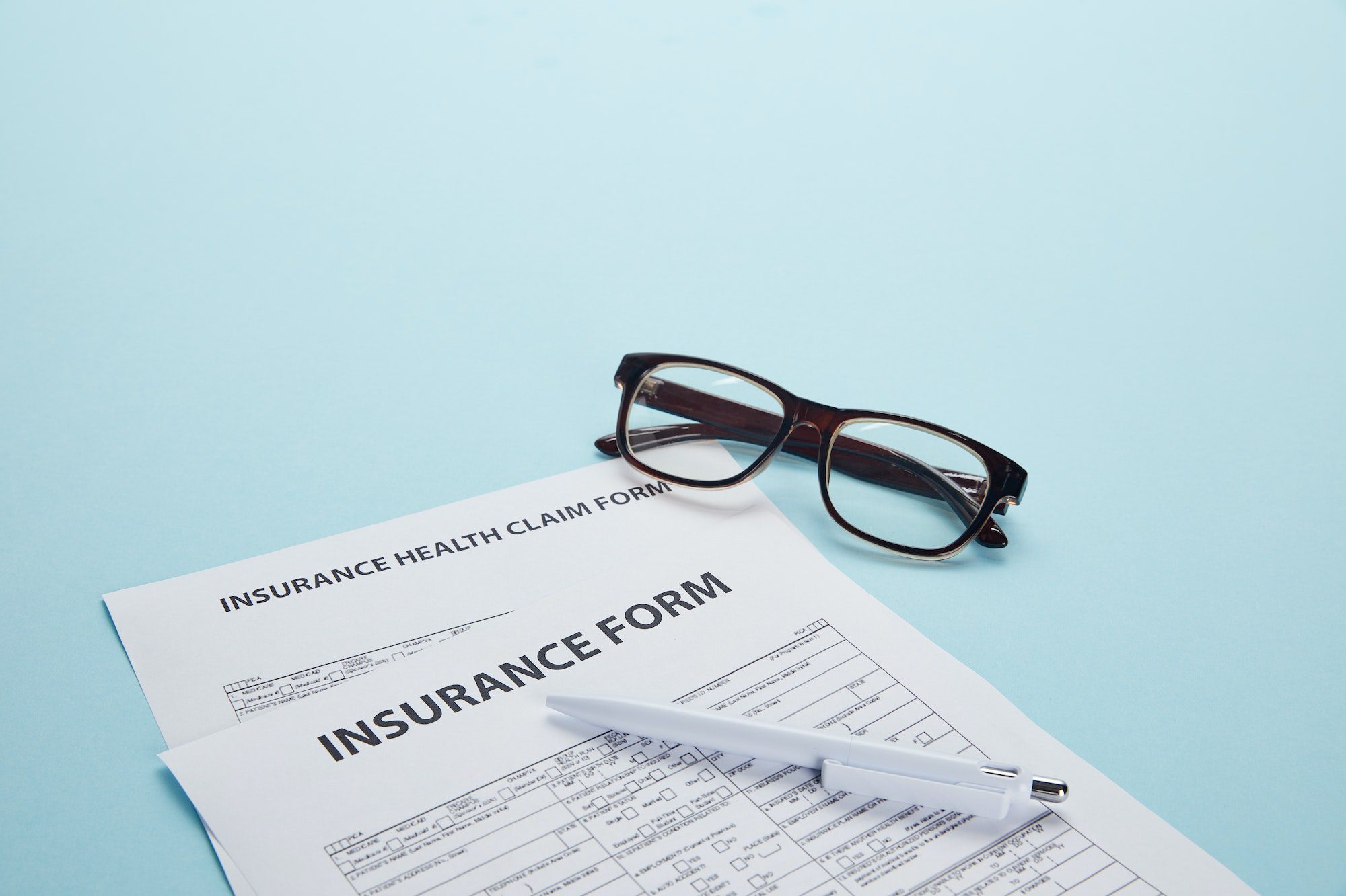 close-up view of insurance form, insurance health claim form, eyeglasses and pen on blue