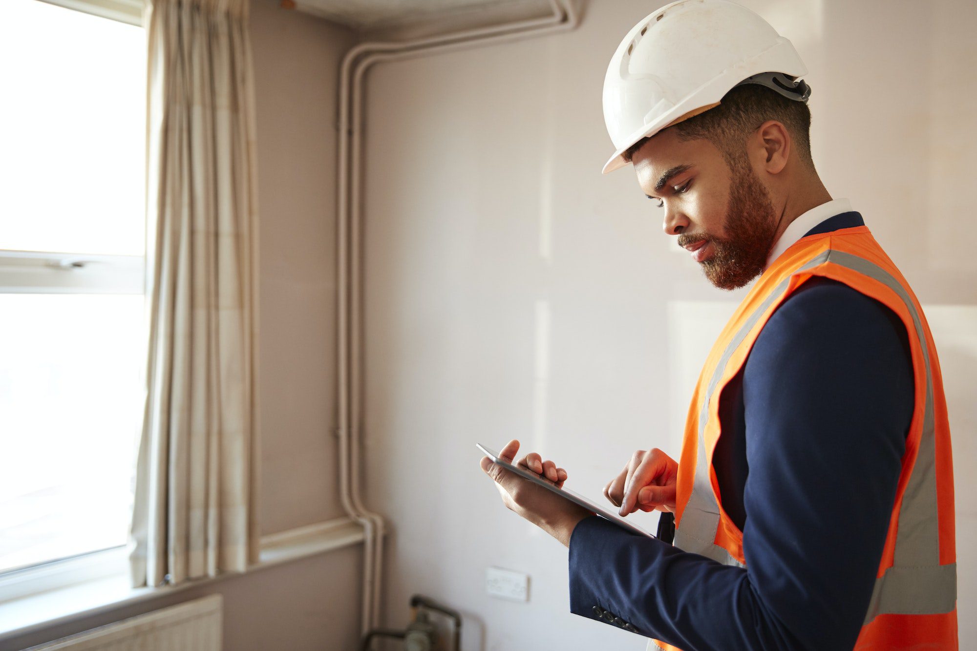 Surveyor In Hard Hat And High Visibility Jacket With Digital Tablet Carrying Out House Inspection