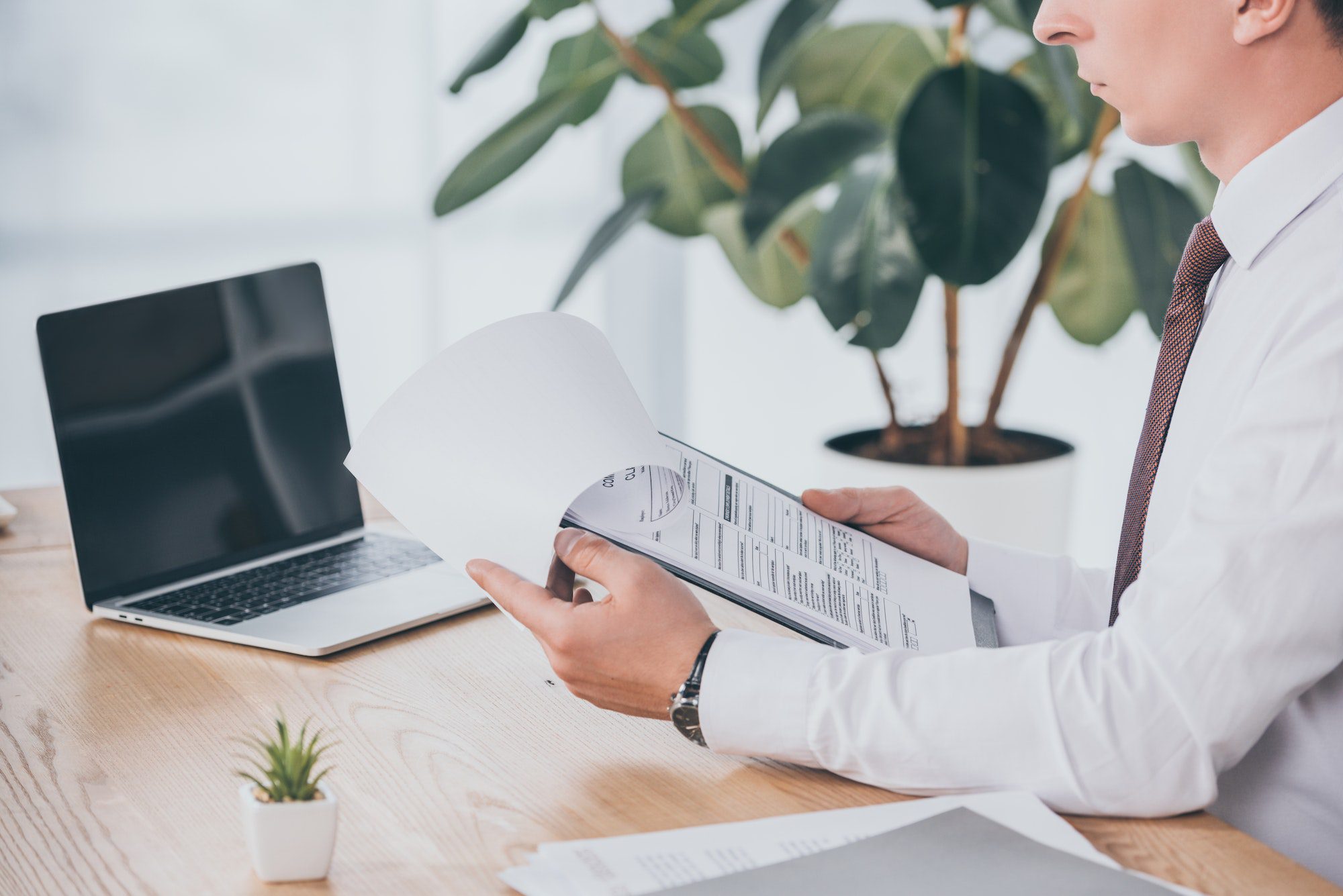 cropped view of businessman reading compensation claim at workplace